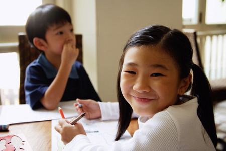 Children sitting at table, girl turning to smile at cameraの写真素材