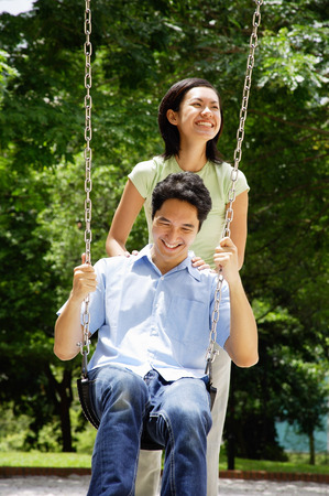 Man sitting on swing, woman standing behind himの写真素材