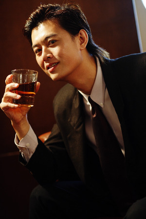 Businessman holding glass of whiskey, looking at cameraの写真素材