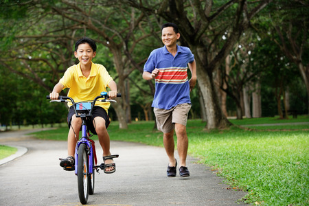 Boy cycling, father running behind himの写真素材