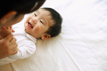 Baby boy lying down, looking up at motherの写真素材