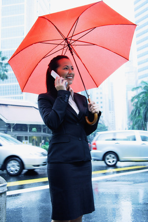 Business woman using mobile phone, holding umbrellaの写真素材