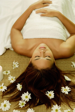 Young woman lying on back, flowers scattered around herの写真素材