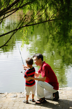 Father teaching son to hold fishing poleの写真素材