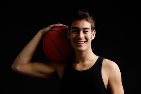 Man holding basketball on shoulder, smiling at cameraの写真素材
