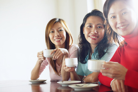 Women sitting at table with cups and saucers, looking at cameraの写真素材
