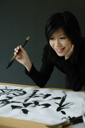 Woman holding paintbrush, looking at Chinese script on paperの写真素材