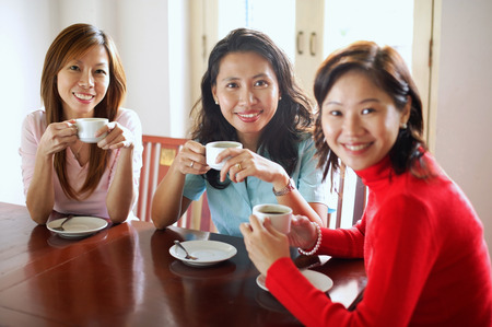 Women in cafe holding cups, smiling at cameraの写真素材