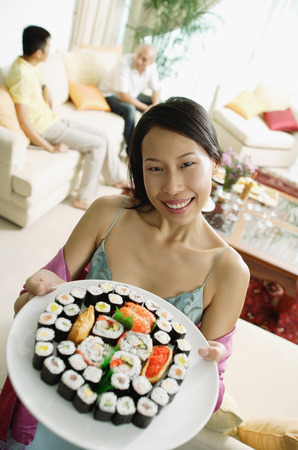 Woman holding up plate of sushi, looking at camera, people in the backgroundの写真素材