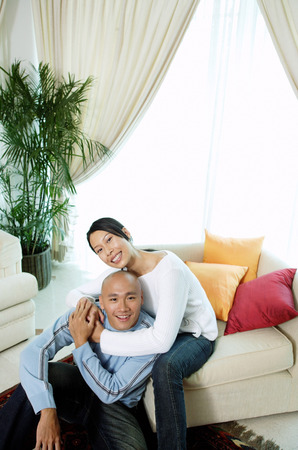 Couple in living room, woman with arm around man, looking up at cameraの写真素材