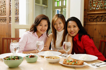 Three women sitting at restaurant table, smiling at cameraの写真素材