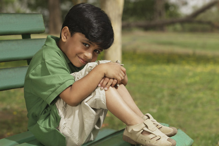 Little boy hugging knees on park benchの写真素材