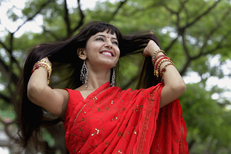 Indian woman wearing red sari smiling with hands in hairの写真素材