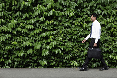 Indian man walking in front of green leafy hedge.の写真素材
