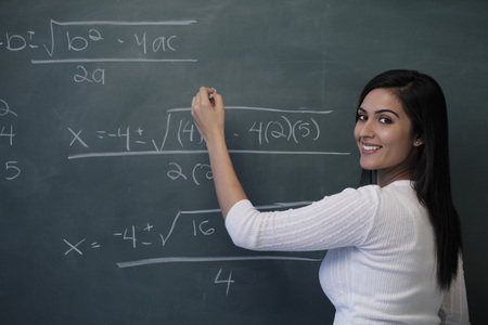 Young woman writing math equation on chalk board and smilingの写真素材