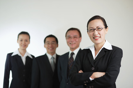 Businesswoman with arms crossed, other executives in the background, smilingの写真素材