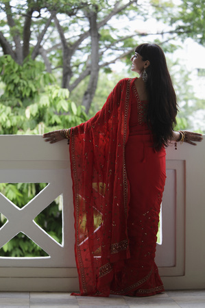 Back shot of Indian woman wearing a red sari looking over balcony.の写真素材