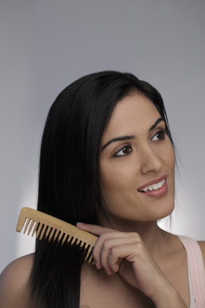 Head shot of young woman combing her long hairの写真素材