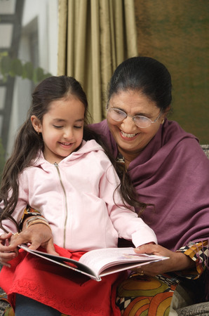 granddaughter sits on grandmother's lap for story (vertical)の写真素材