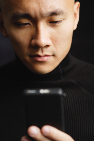 Man with shaved head, looking at mobile phone, selective focusの写真素材