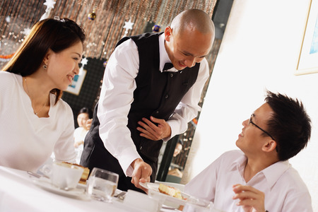Waiter serving customers in restaurantの写真素材
