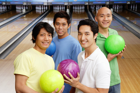 Four men in bowling alley, holding bowling ballsの写真素材
