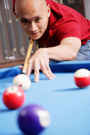 Man holding pool cue, aiming at ball