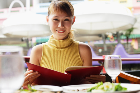 Woman holding menu, looking at camera, smilingの写真素材