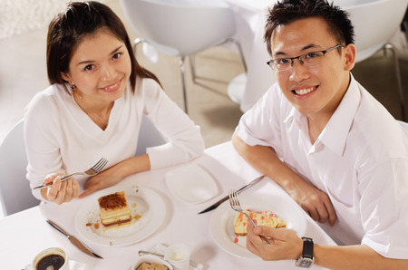 Couple eating dessert in restaurant, looking up at cameraの写真素材