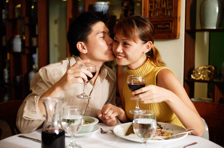 Couple in Chinese restaurant, holding wine glasses, man kissing woman on cheekの写真素材