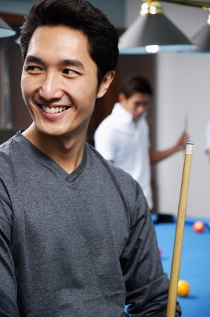 Man holding pool cue, smiling, looking awayの写真素材