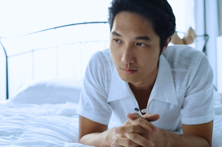 Man lying on bed, hands claspedの写真素材