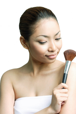 Woman holding make-up brush, looking awayの写真素材