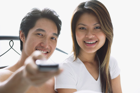 Couple sitting on bed, man holding remote towards cameraの写真素材