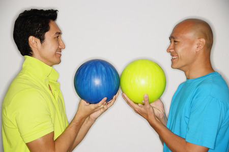 Two men standing face to face, carrying bowling balls, smilingの写真素材