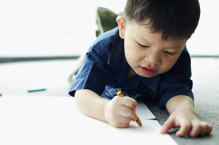 Young boy lying on floor, drawing with crayonの写真素材