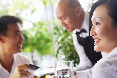 Woman looking away, man paying with credit card bill in the backgroundの写真素材