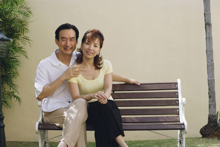 Mature couple sitting on bench, smiling at cameraの写真素材