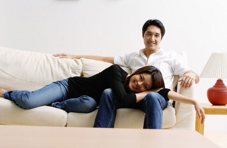 Couple on sofa, woman lying on mans lap, looking at cameraの写真素材