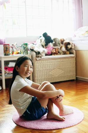 Girl in bedroom, sitting on floor, hugging kneesの写真素材