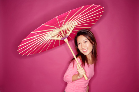 Woman with umbrella, standing against pink backgroundの写真素材