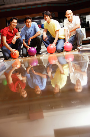 Four men in bowling alley, crouching, holding bowling ballsの写真素材
