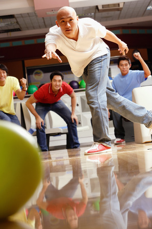 Man bowling, friends in the background, cheeringの写真素材