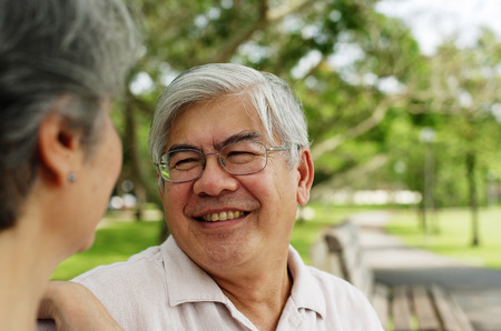 Mature couple sitting in park, facing each other, man smilingの写真素材
