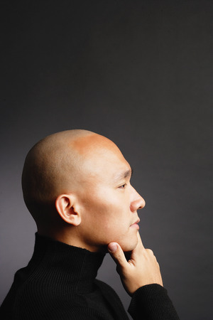 Man with shaved head, hand on chin, looking awayの写真素材
