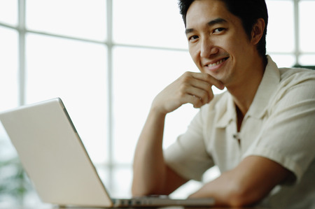 Man with laptop, smiling at camera, hand on chinの写真素材
