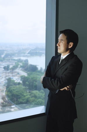 Businessman standing next to window, arms crossedの写真素材