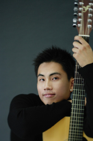 Young man dressed in black leaning on guitar