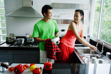 Couple standing in kitchen, woman washing hands, man drying dishesの写真素材
