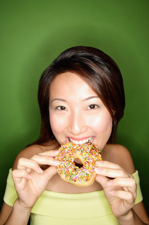Woman biting into donut, looking at cameraの写真素材
